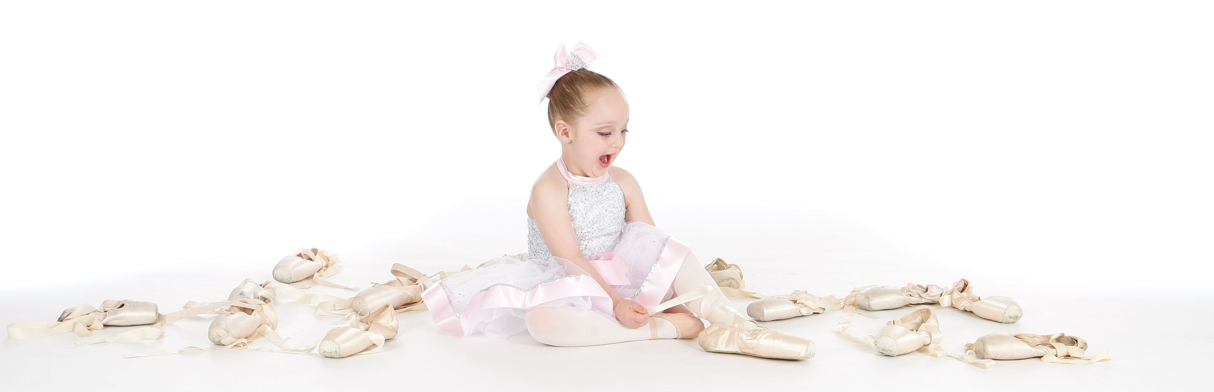 little girl playing with ballet point shoes dressed in pink